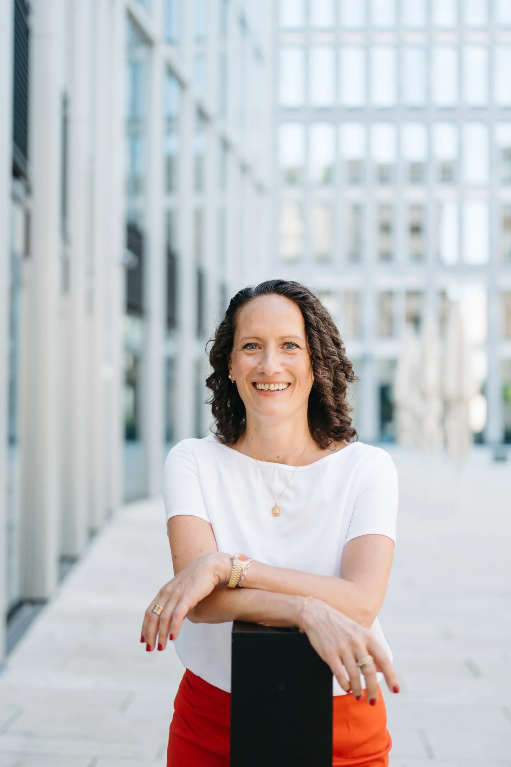Portrait von Mirjam Berle vor einem hellen Hochhaus mit weißem Shirt und roter Hose